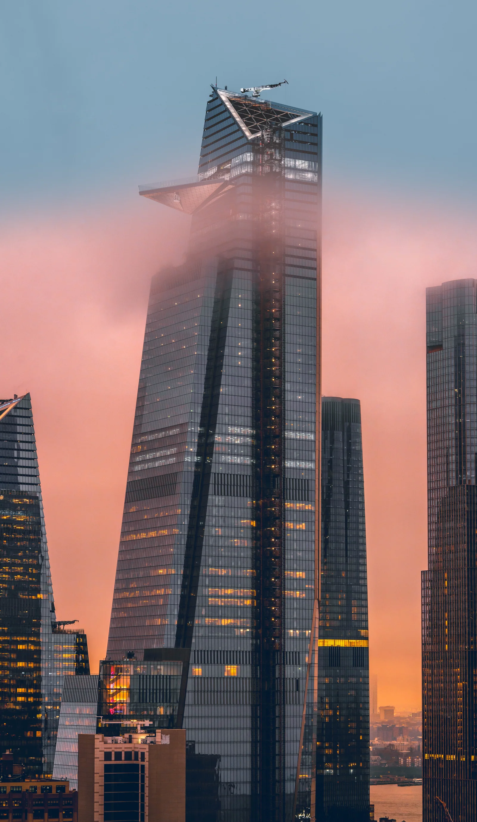 A glass skyscraper rises through pale pink clouds above the city.
