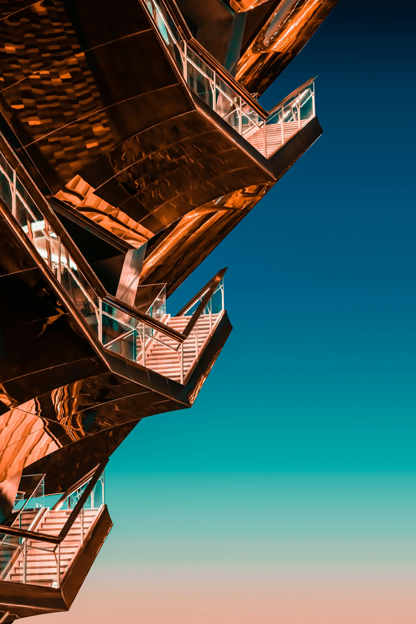 Orange fire escapes climb between tall buildings toward a turquoise sky.