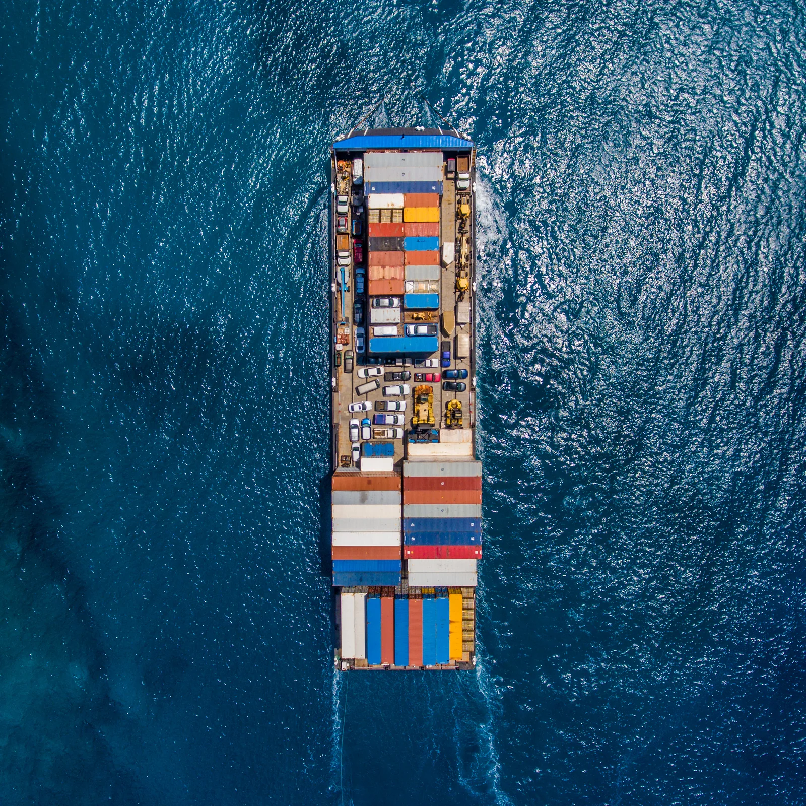 An overhead view of a container ship carrying rows of brightly colored containers across deep blue water.