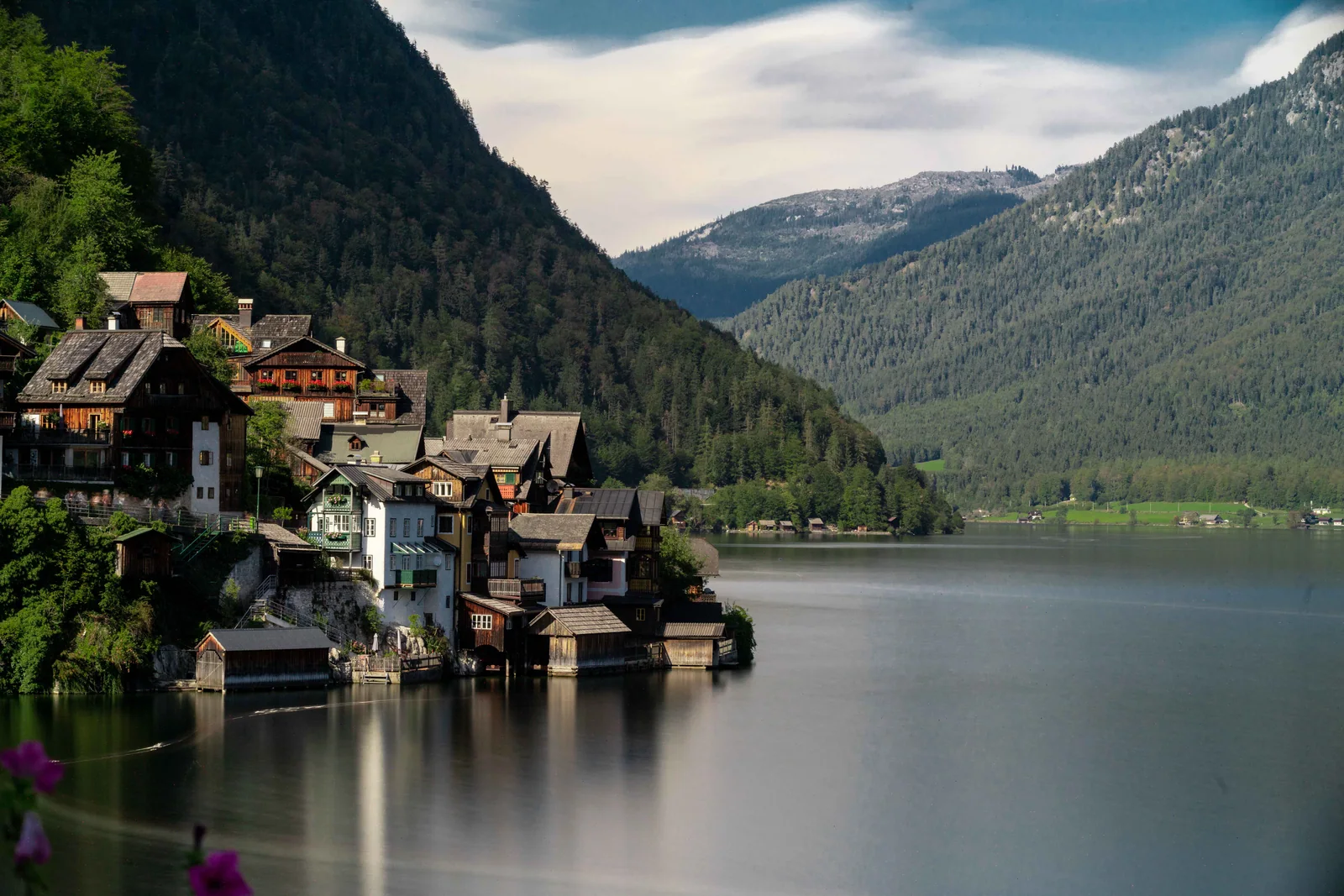 A lakeside village, church spire, and clustered rooftops sit below forested mountains.