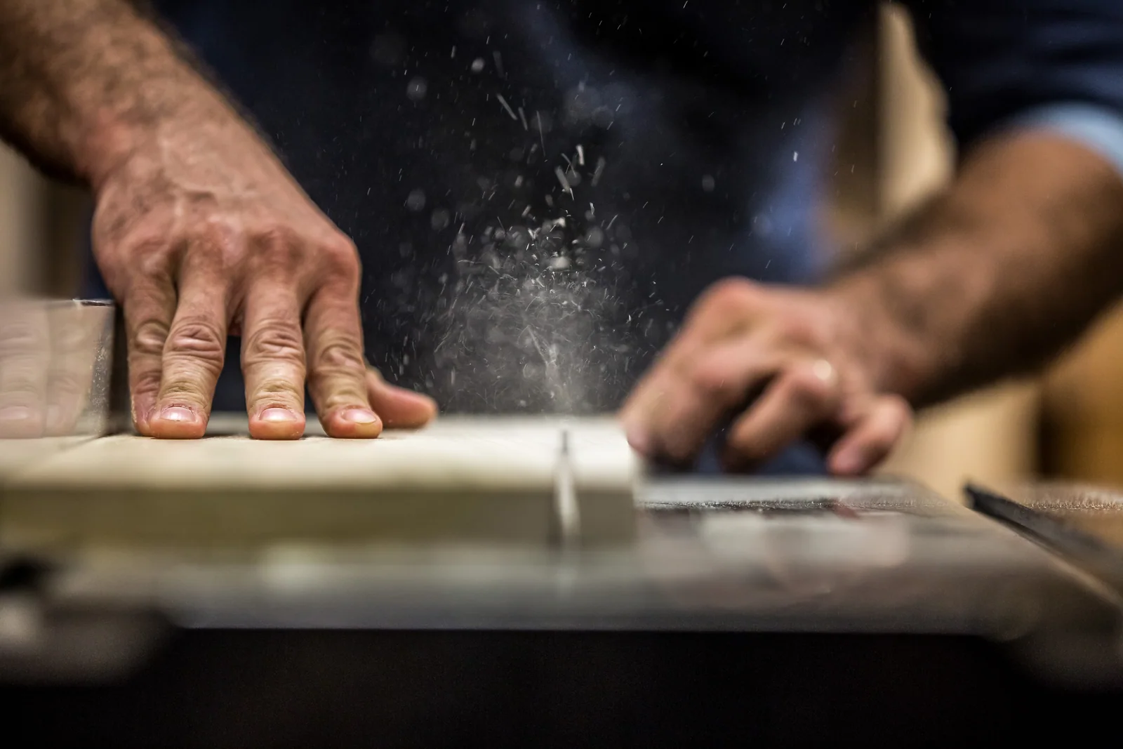 Working hands move through a cloud of pale dust above a worn work surface.
