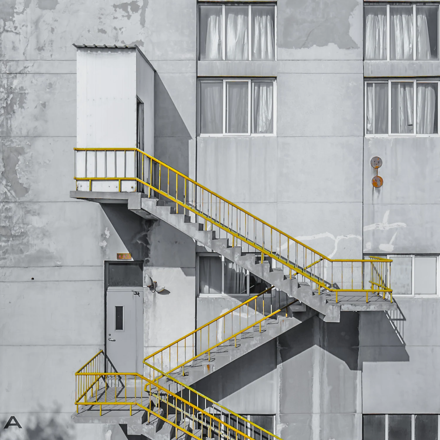 A bright yellow stair railing zigzags across a gray concrete building.