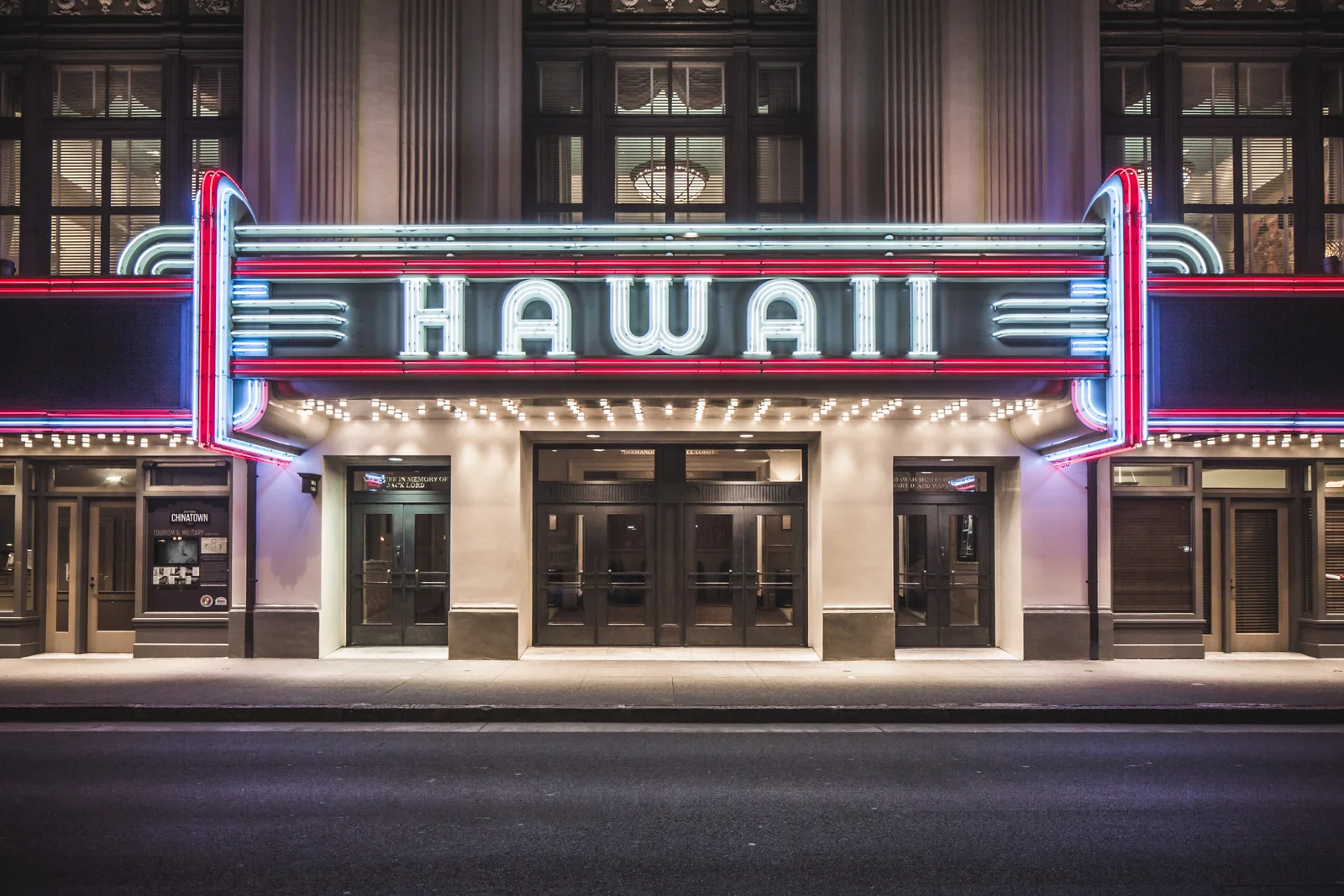 An illuminated HAWAII theater marquee glows red and turquoise above an empty nighttime sidewalk.