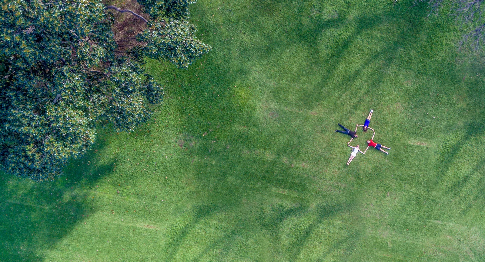 Three people lie with their arms and legs spread on a green lawn, seen from directly above.
