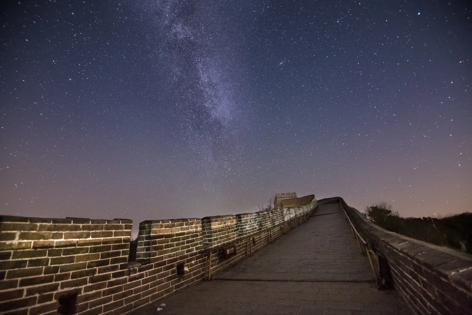An old stone wall winds over a hillside beneath a star-filled night sky and the Milky Way.