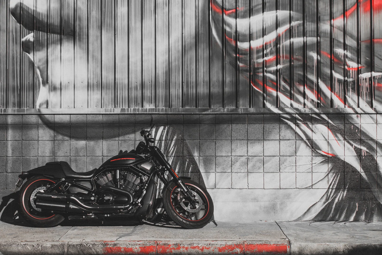 A black motorcycle stands beneath a large black-and-white face mural with small red accents.