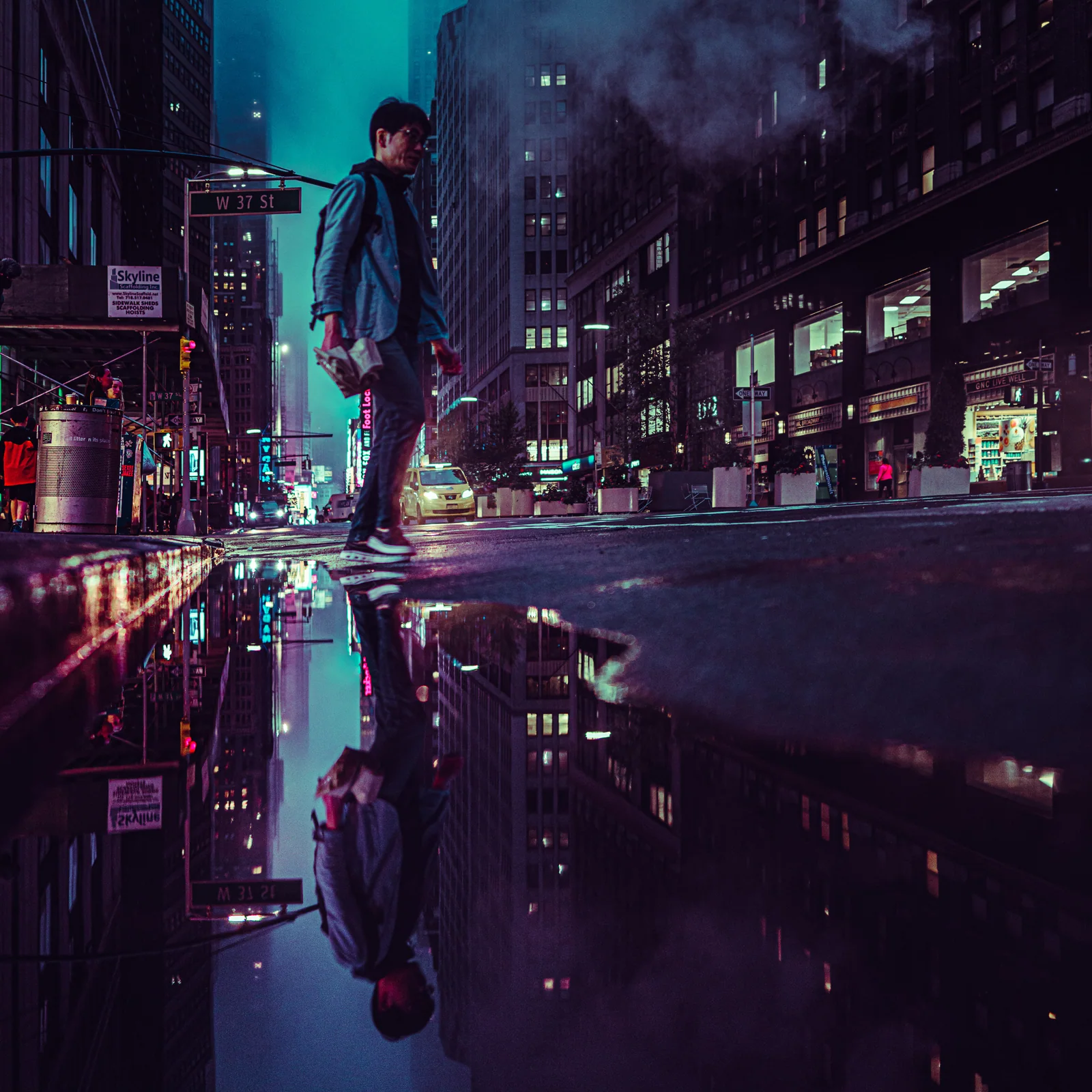A person stands at a neon-lit street corner, mirrored in a still puddle below.